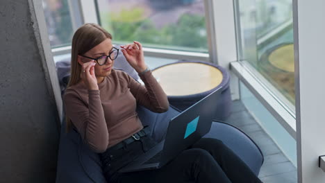 young lady working on laptop. tired freelancer puts off her glasses, closes computer and looks into window smiling. high angle view.