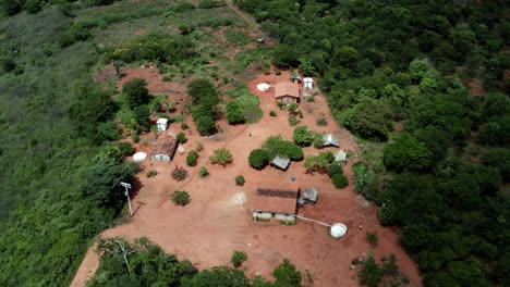 rotating aerial drone shot of a brazilian farm in the chapada diamantina national park in northern brazil with various houses surrounded by green trees, red dirt, and a man walking around