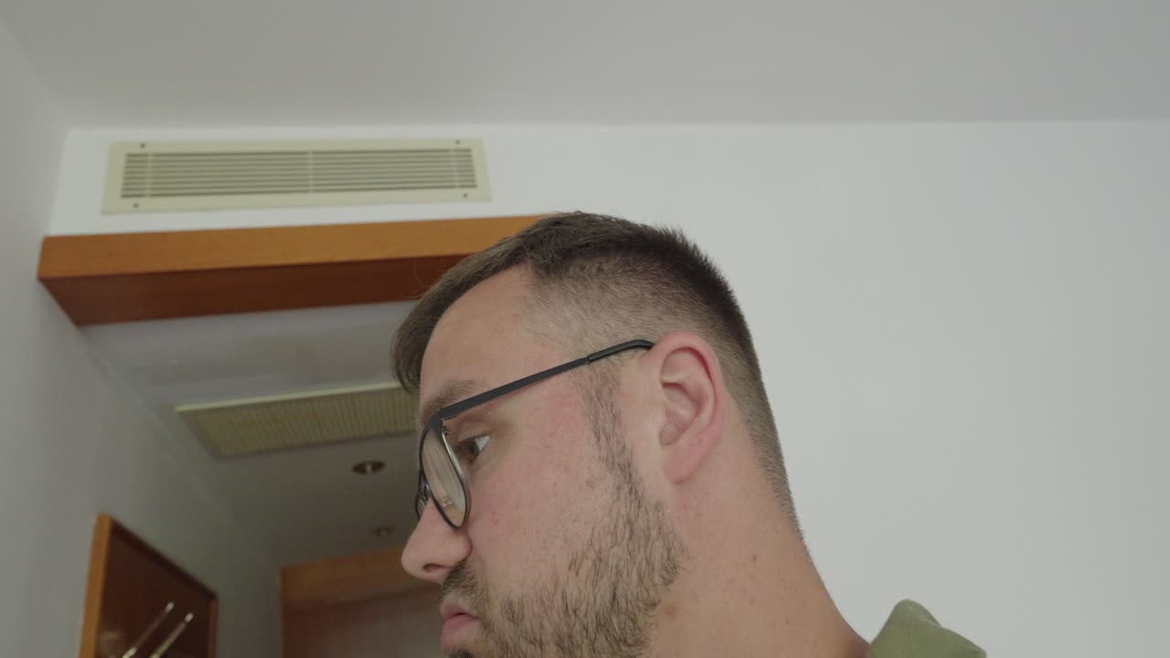 A man in a hotel room waves his hands in front of his nose, reacting to an unpleasant odor coming from the air conditioner or ventilation