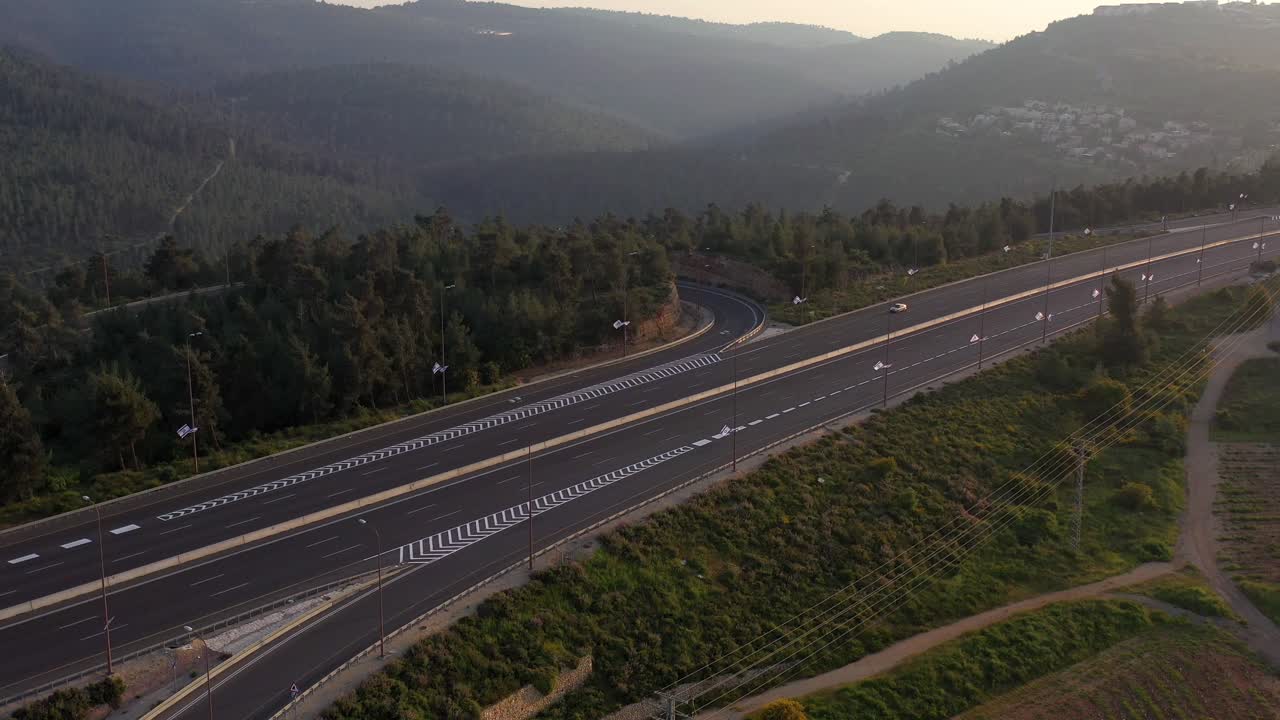 Aerial view of a winding highway through a forested mountain landscape at sunrise