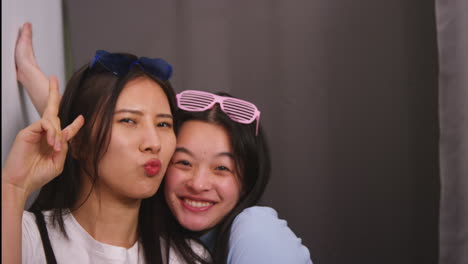 two female friends in photo booth wearing cool glasses having fun posing for portrait and pulling faces in real time 2