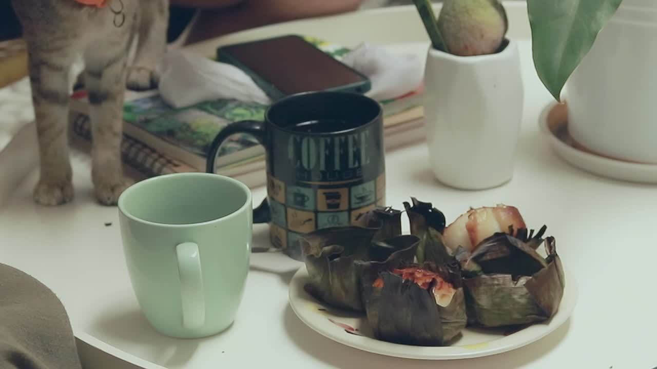 Cheeky kitten sniffing around the table while owners are having bibingka or filipino rice cake and coffee for merienda that shows the candid adorable home moment with a pet