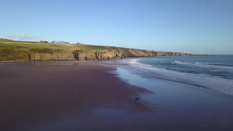 Luftaufnahmen-Eines-Paares,-Das-An-Einem-Sonnigen-Tag-In-Lunan-Bay,-Angus,-Schottland,-Am-Strand-Spazieren-Geht