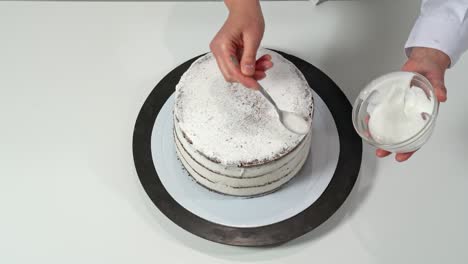 top view of a baker pouring melted white chocolate on the edges of the cake so it drips down the sides.