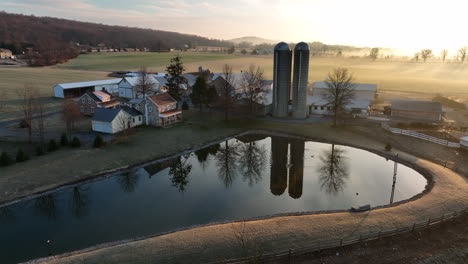 Wunderschöne-Bauernhofszene-Im-Winterlichen-Sonnenaufgangslicht,-Das-Sich-Im-Teich-Spiegelt