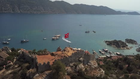 seaside simena castle ruins on rocky hill flying turkish flag, aerial
