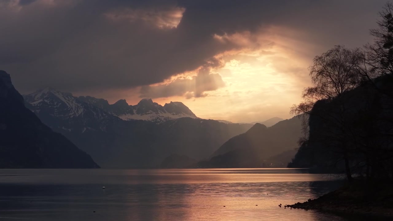 Cinematic aerial view of Walensee at sunset with dramatic clouds, alpine mountains and golden reflections on lake.