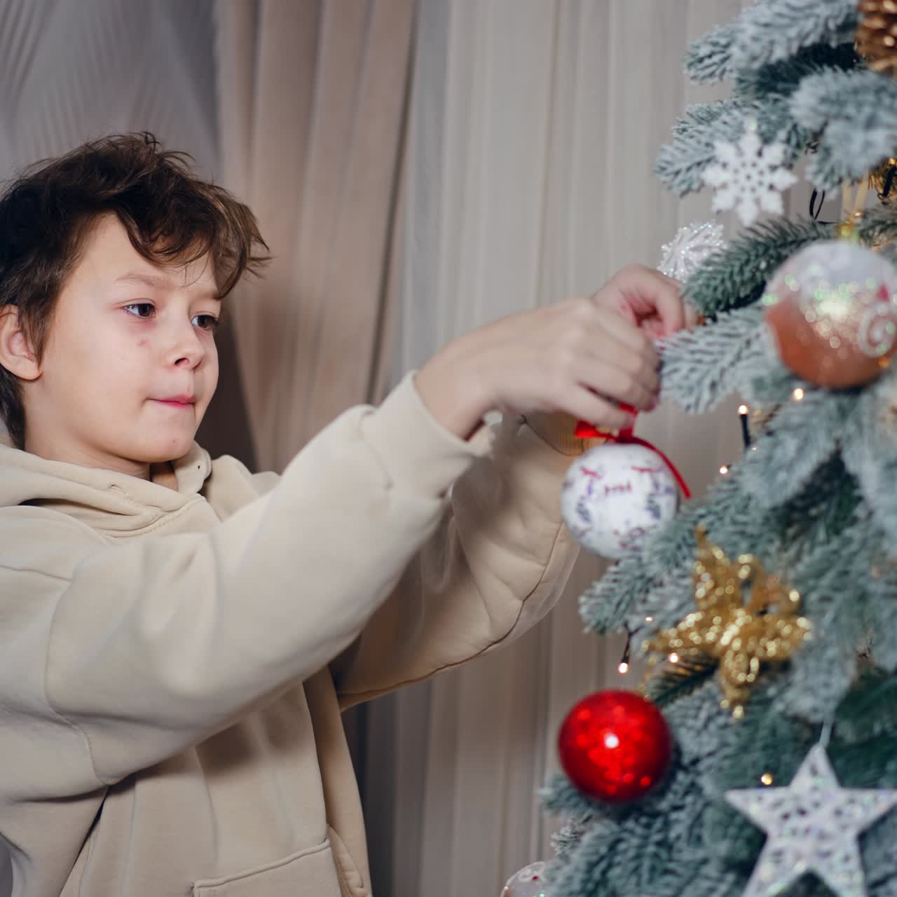 Dark-haired Caucasian boy decorating the Christmas tree. Teenager wants to hang the ball but he can't