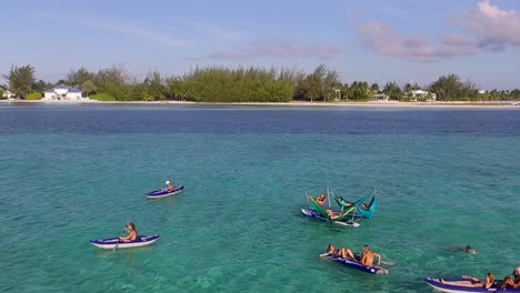 drone flies over hammocks on wakeboards and kayakers paddling in clear turquoise water
