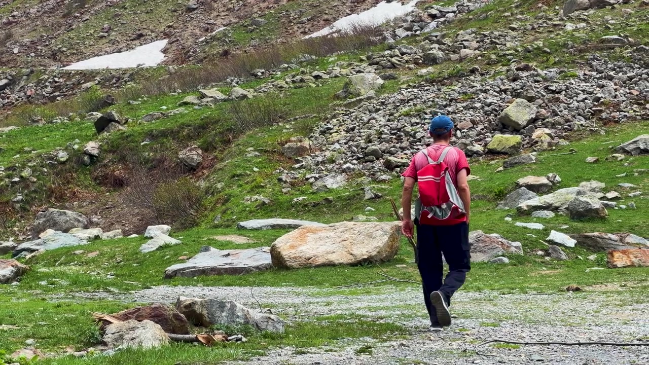 Un escursionista si allontana su un sentiero di montagna roccioso sotto la luce intensa del giorno in Italia