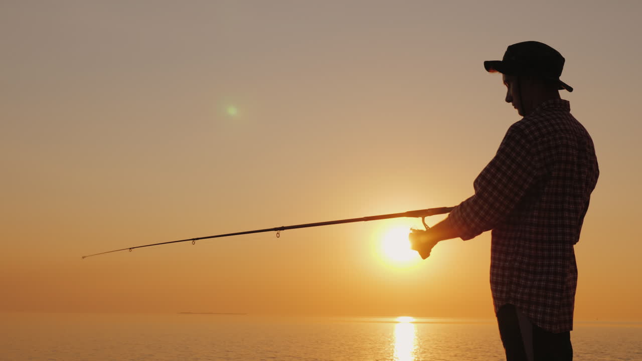 Siluet Nelayan Muda Memancing di Pantai Saat Matahari Terbenam, Video 4K