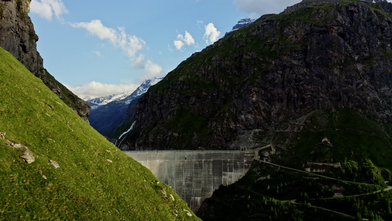 Stunning FPV and drone shots soaring through the Swiss Alps, capturing the Mauvoisin Dam and its majestic waterfall on a clear, sunny summer day.