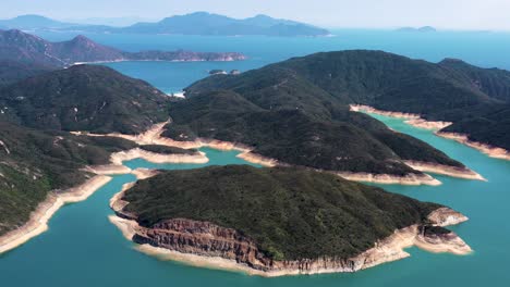 aerial orbit of high island reservoir rock columns in verdant hills shore and turquoise water, san kung peninsula in hong kong, china