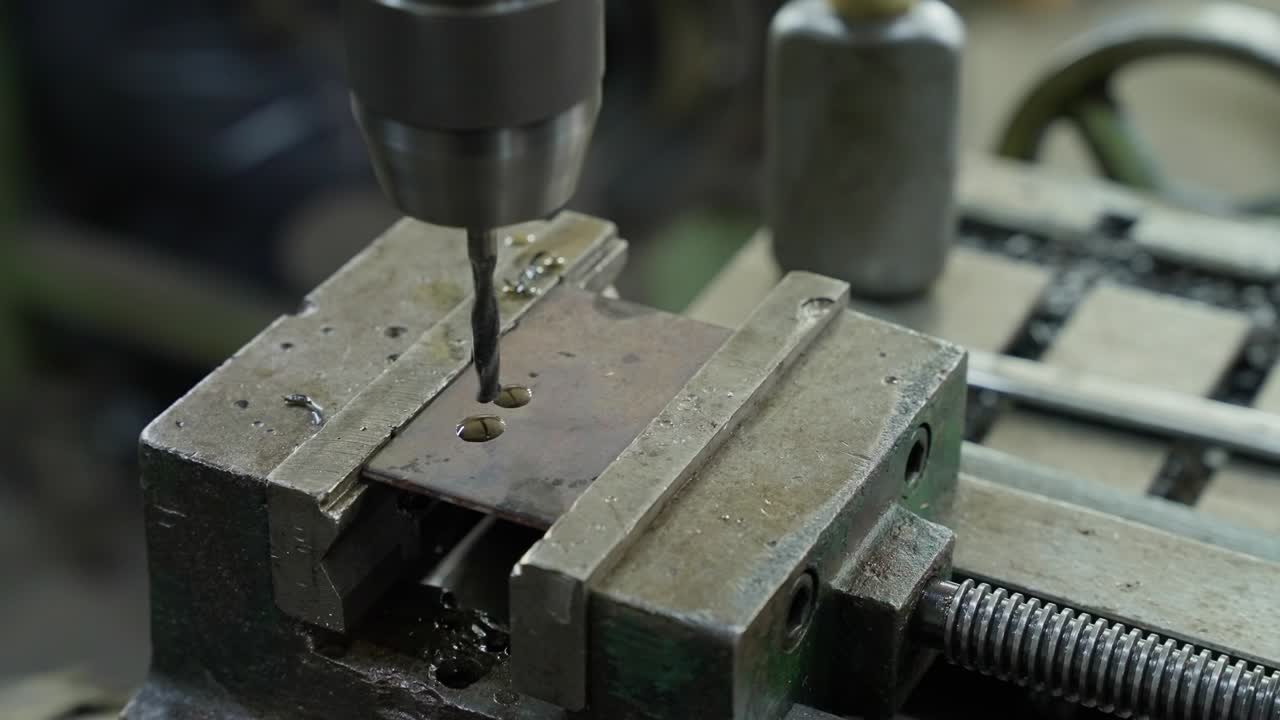 close up of drill press piercing steel plate held by heavy duty vise in workshop setting