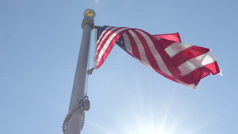 an american flag blowing in the wind in front of the sun