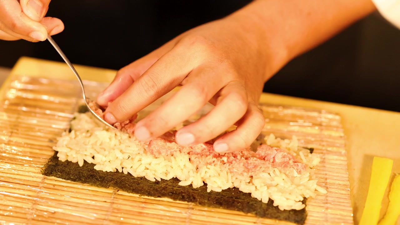 巻きすの上でご飯にマグロをスプーンで広げるシェフのクローズアップ