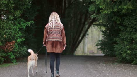 Una-Chica-Rubia-Camina-Por-La-Calle-Con-Su-Perro-Atado-En-Un-Día-Frío-Y-Nublado