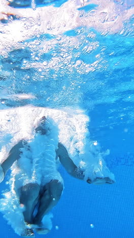 an energetic dive into a swimming pool. handsome young man swimming in pool, underwater view vertical video