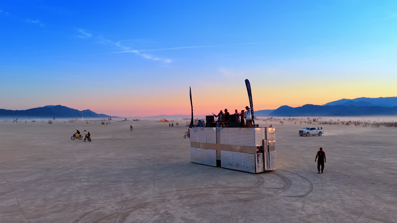 California, USA, 1 luglio 2025: Auto d'arte riflettente e ciclisti a un festival d'arte nel deserto. Vista ravvicinata di un veicolo mutante a specchio e persone in bicicletta sul terreno piatto della playa durante l'ora d'oro.