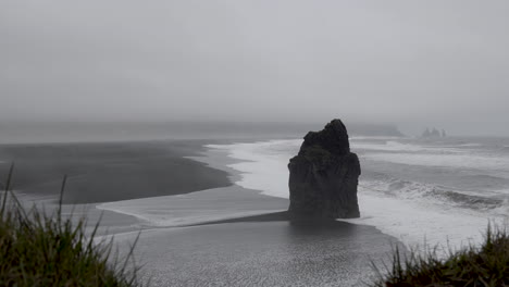 Waves-Splashing-Onto-Rough-Black-Boulder-Near-The-Shore-In-Reynisfjara-Black-Sand-Beach-In-Iceland-With-Foggy-Background