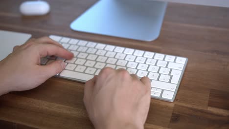 hands typing on computer keyboard sitting at home office desk