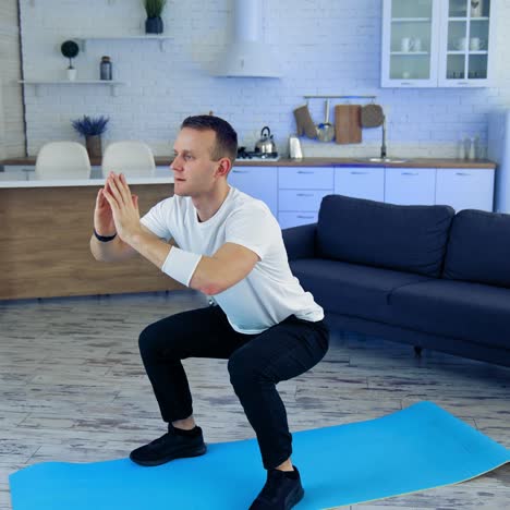 young man exercising on fitness mat at home. active male in white t-shirt and black pants doing his workout on quarantine on kitchen background. sport, fitness and healthy lifestyle at home