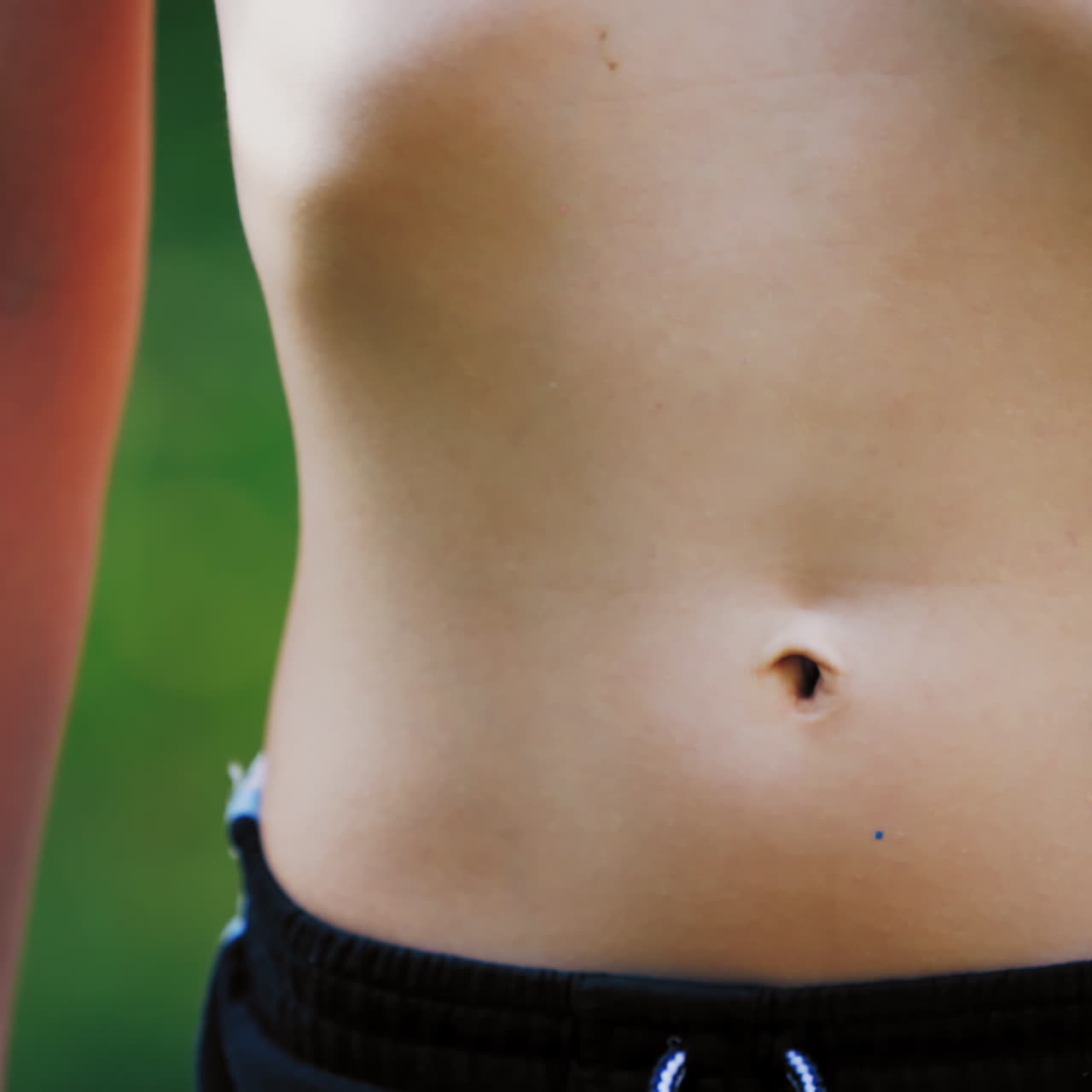 Bare stomach of a young boy outdoors. Healthy boy in sport pants does exercises breathing by his belly. Close-up.