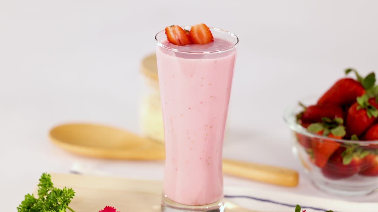 Batido de fresa rosa en vaso, iluminación brillante, cámara estática, frutos rojos frescos y accesorios de cocina