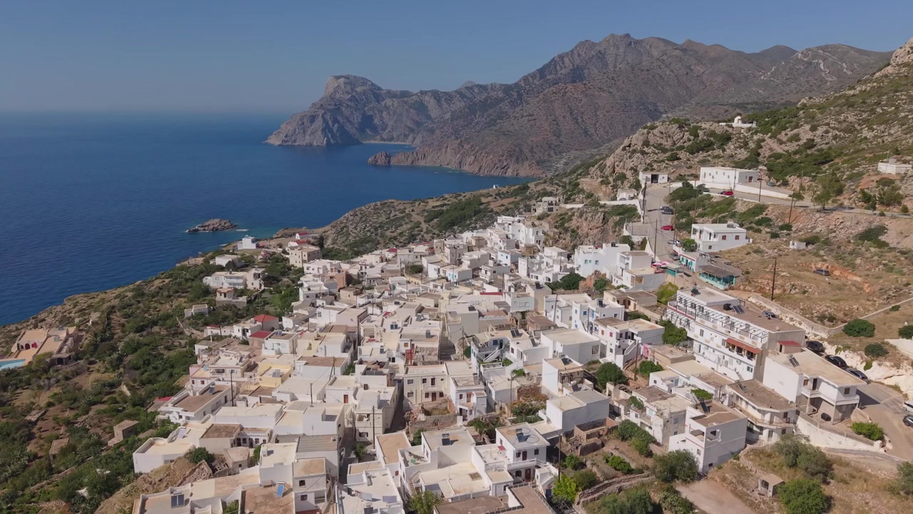 Drohnen-Zoomfahrt enthüllt das traditionelle Dorf Mesochori auf Karpathos, mit zerklüfteten Bergen und der tiefblauen Ägäis, die eine spektakuläre Inselkulisse schaffen