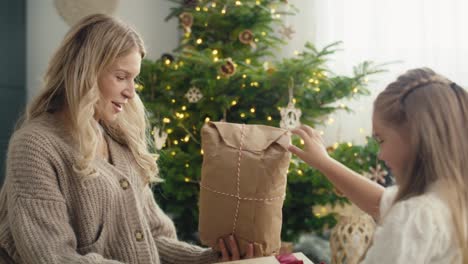 side view of caucasian girl and mother giving and receiving christmas gifts on the floor.