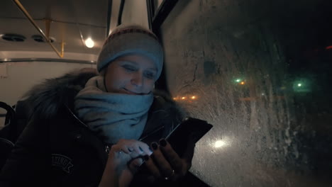 mujer con móvil viajando en autobús en la noche de invierno