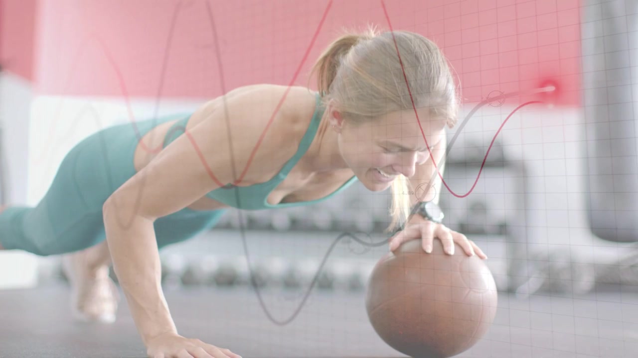Woman reaching for brown medicine ball in gym, alternating push-ups for core, graph lines tracking