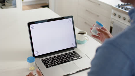 hombre biracial sosteniendo medicamentos haciendo una llamada de video usando una computadora portátil, copia el espacio en la pantalla, cámara lenta