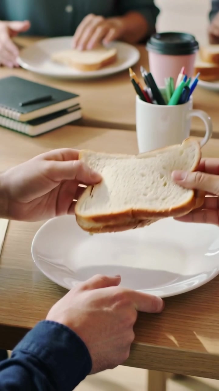 Vertical video: Reaching hands in denim placing two slices white bread on plate at table, for break