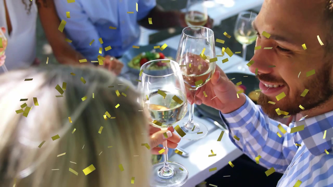 Donna che alza un bicchiere, un gruppo che brinda a un lungo tavolo, coriandoli animati che cadono festeggiando la cena.