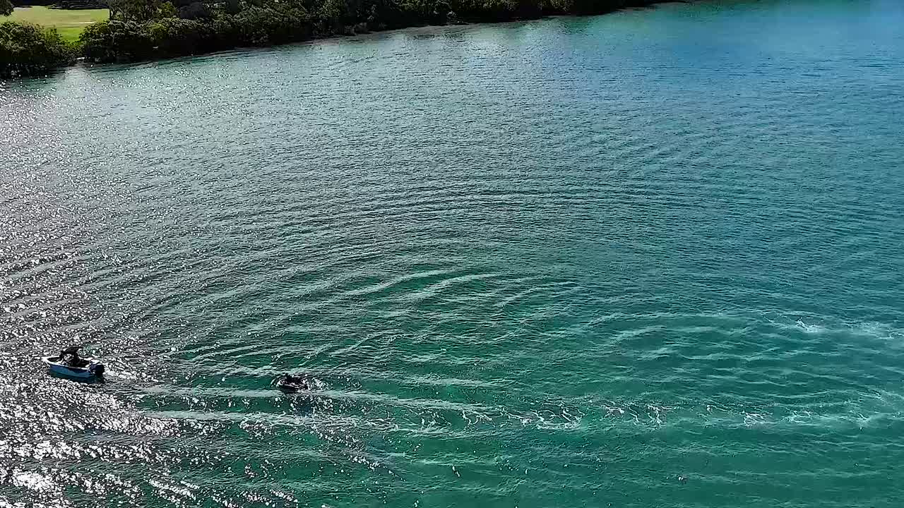 A jet ski moves across a clear river, leaving ripples in its wake under a sunny sky.