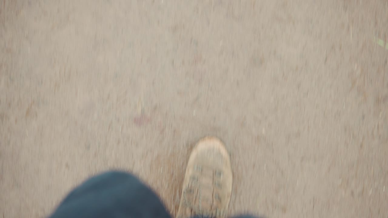 Spor ayakkabı ve kot pantolonlu yürüyen bir kişinin FPV aşağıdan görünümü.