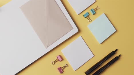 overhead view of notebook, pens and stationery arranged on yellow background, in slow motion