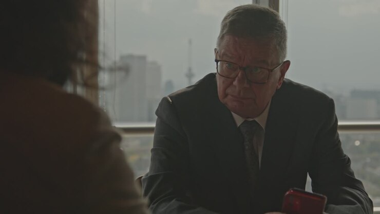 An older businessman sits across a business partner in an office and talks