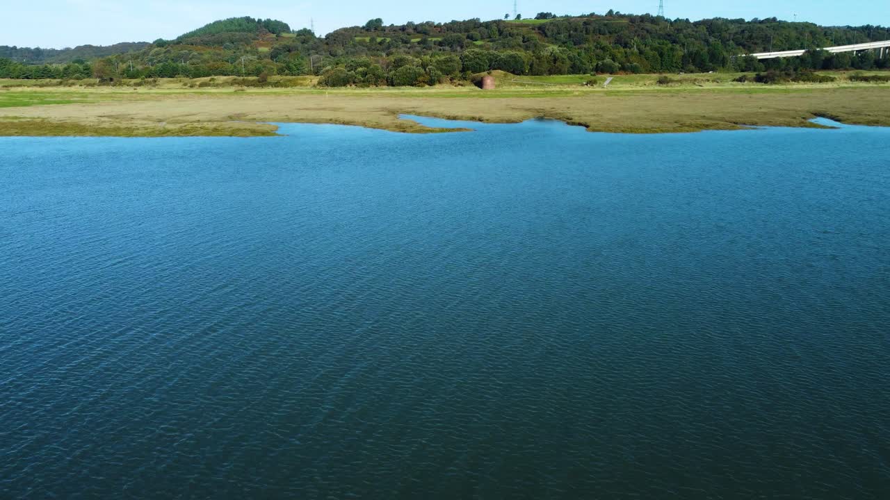 Fast Moving Drone Shot Over Calm Beautiful Blue Water with Wetlands and Forest with Road in Background