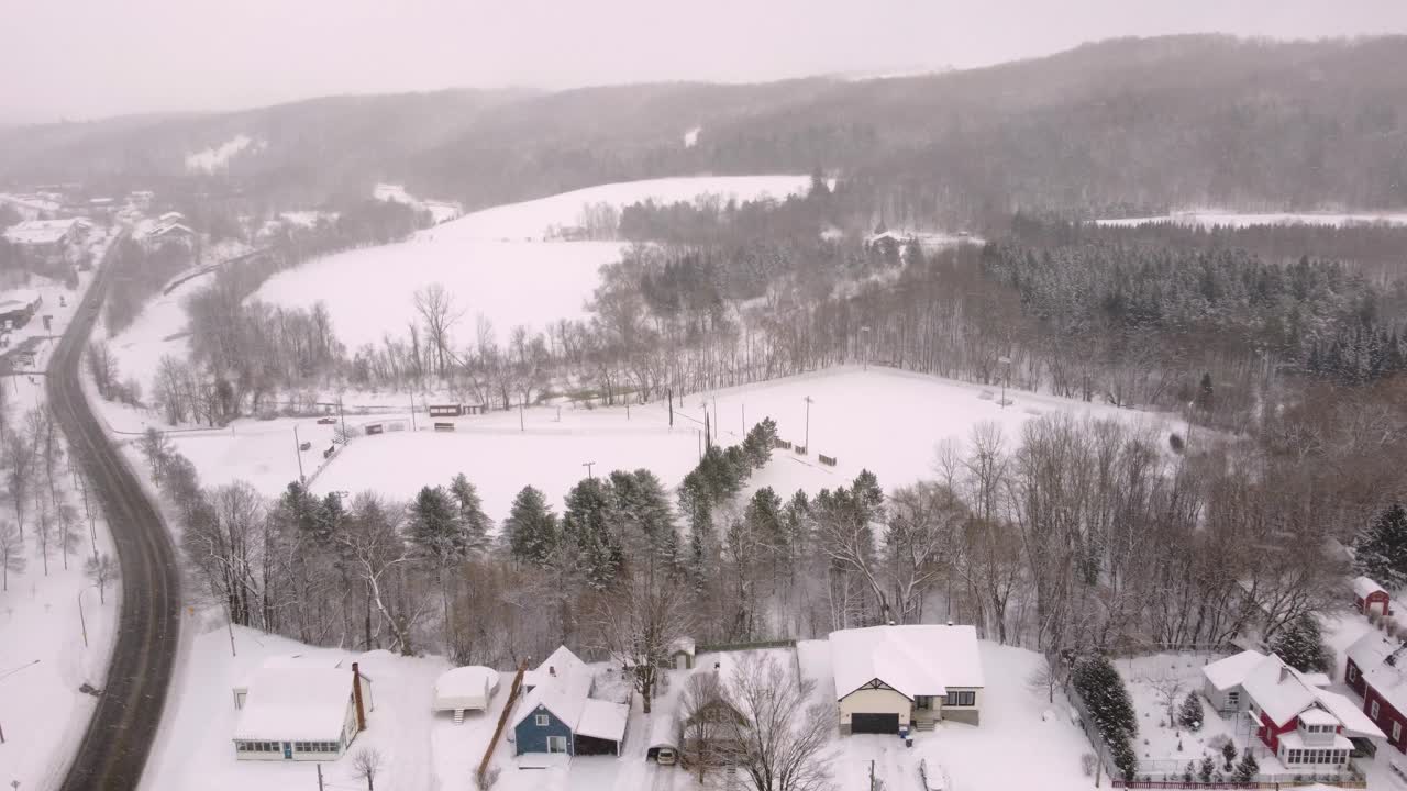 A serene winter view over Sherbrooke, Canada, showing snow-covered homes, winding roads, and surrounding hills and forest. A calm, overcast atmosphere highlights rural cold-season charm.