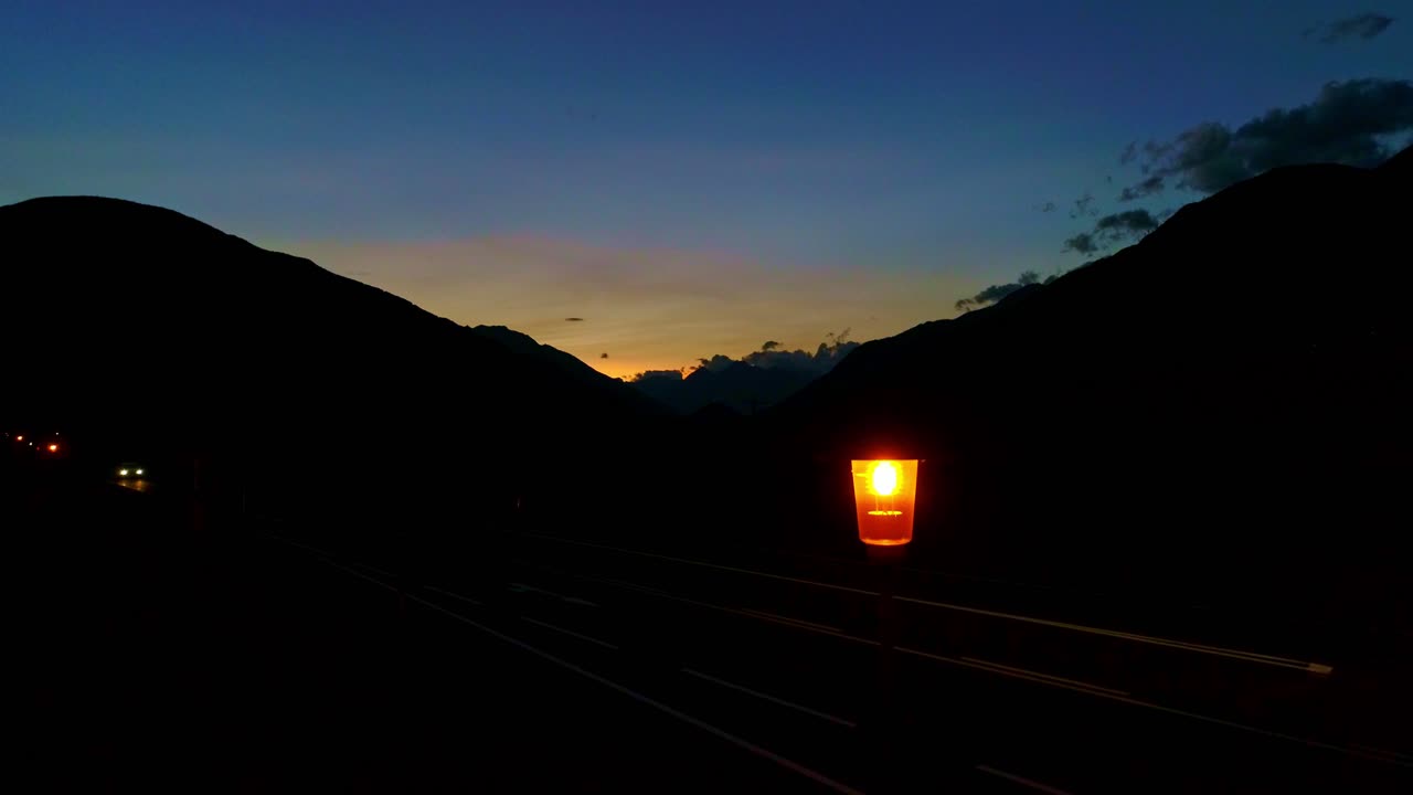 Evening scene of mountain road, where single streetlamp glows, twilight sky, drone