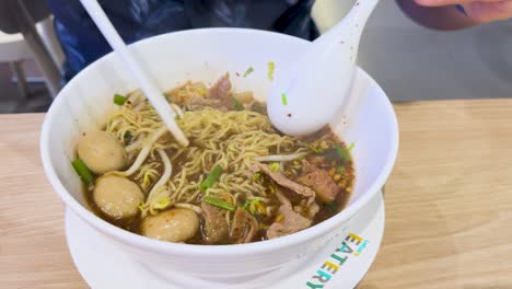 mixing beef noodles with broth and toppings