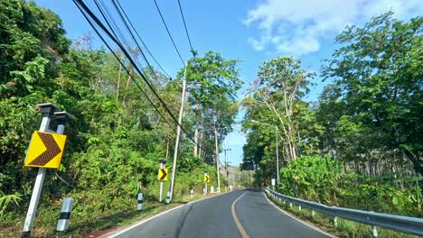 a 19-second drive along a verdant road in phuket, thailand, showcasing vibrant greenery and clear blue skies