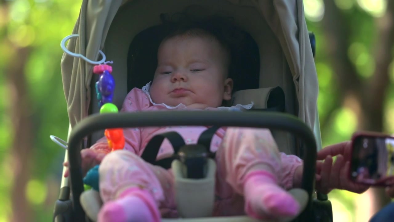 Young mother gently interacting with her infant seated in a stroller during an outdoor walk