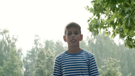 Niño-Con-Ojos-Azules-Y-Una-Camisa-A-Rayas-Lanza-Una-Pelota-De-Fútbol-Y-La-Toca-Con-La-Cabeza-En-El-Parque