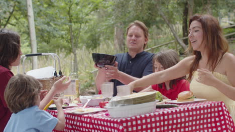 feliz familia caucásica haciendo un picnic en el bosque, comiendo y pasando tiempo juntos