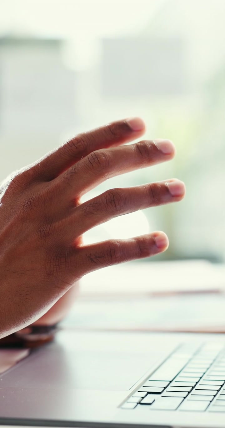 Person Gesturing While Working on Laptop in Office