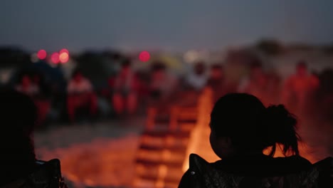 Beach-bonfire-blazing-as-silhouettes-look-on-from-camp-chairs-in-4k-slow-motion