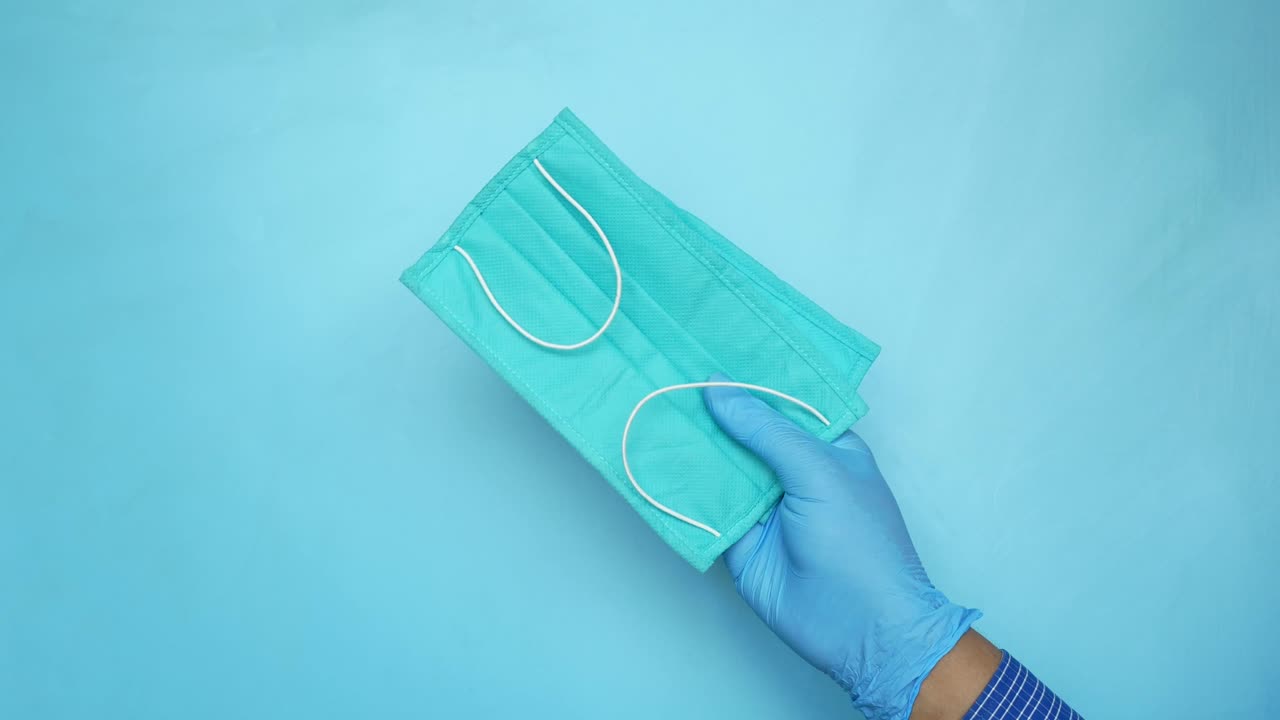 mano con una máscara facial de color azul claro con guantes azules